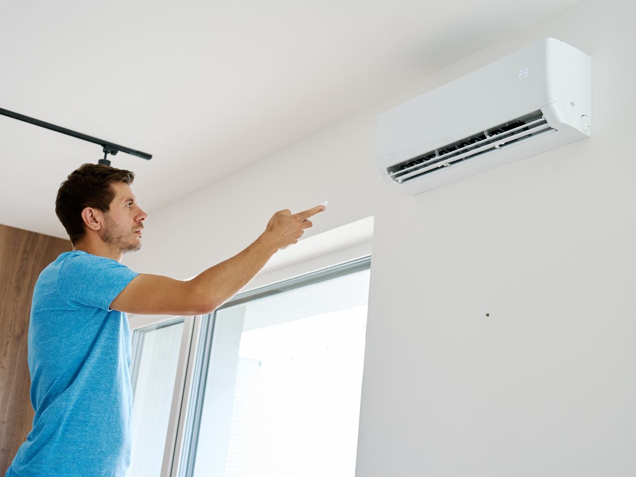 Man adjusting a wall-mounted, undersized air conditioner with a remote control indoors in West Chester, PA